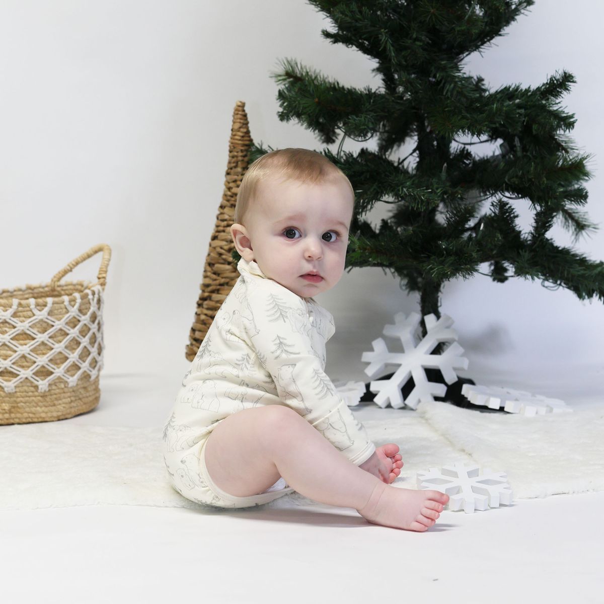 Baby wearing an organic cotton long sleeve bodysuit with polar bear print sitting by a Christmas tree.