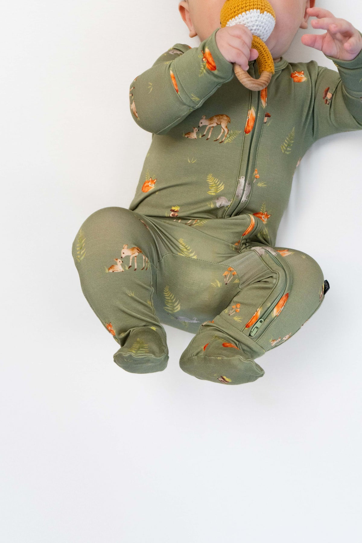 Baby wearing a forest friends footed zipper sleeper with woodland animal print, sitting and chewing a teething toy.