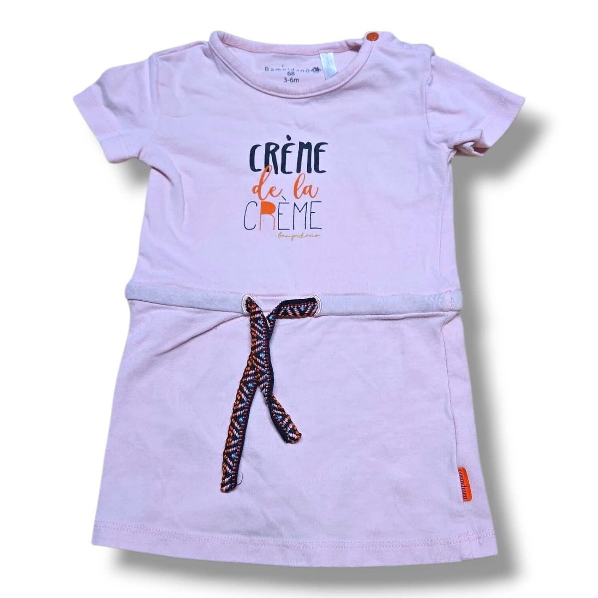 Pre-loved baby dress 3-6 months in soft blush pink with 'Crème de la Crème' graphic and braided waist tie.