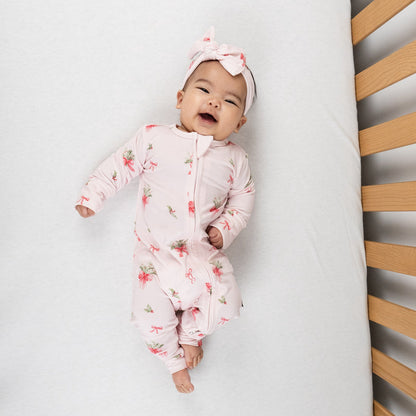 Baby wearing a bamboo footless sleeper pink bows with a pink bow headband, smiling in a crib.