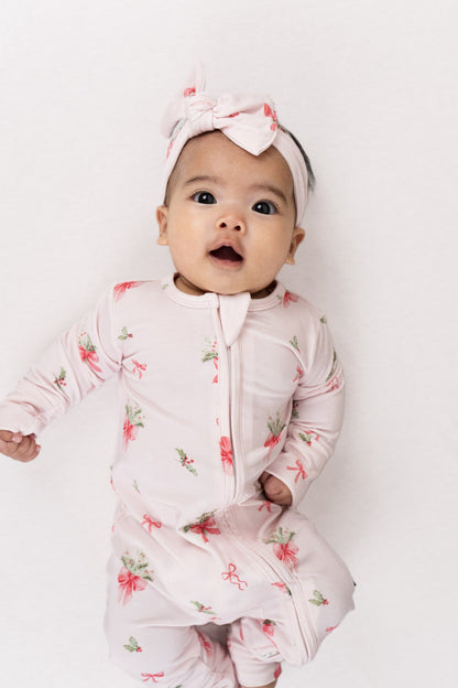 Baby wearing a bamboo footless sleeper pink bows, showcasing a charming Christmas print with pink bows and greenery.