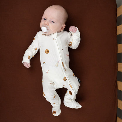 Baby in ribbed bamboo sleeper for babies with cookie and milk print on a brown crib mattress.