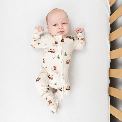 Baby wearing Christmas train bamboo sleeper with charming red train print and soft neutral tones.