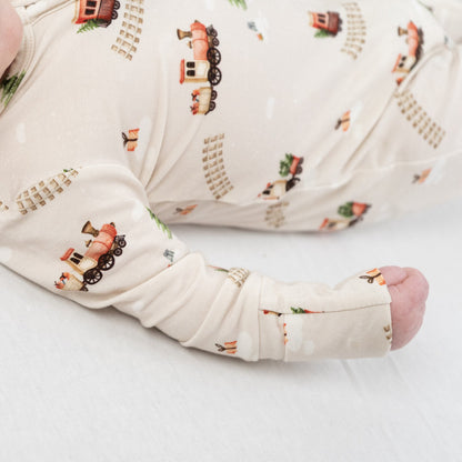 Baby wearing Christmas train bamboo sleeper with whimsical train print and soft tones.