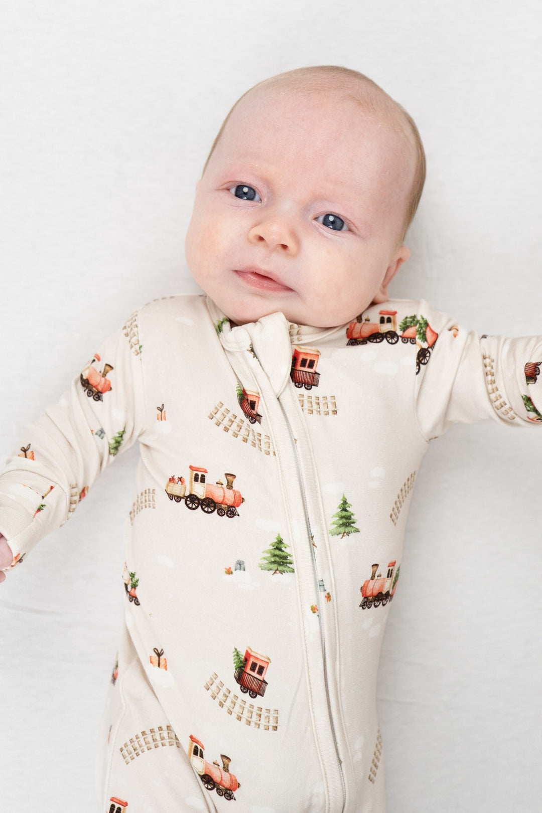 Baby wearing a Christmas train bamboo sleeper featuring colorful train prints and festive winter themes.