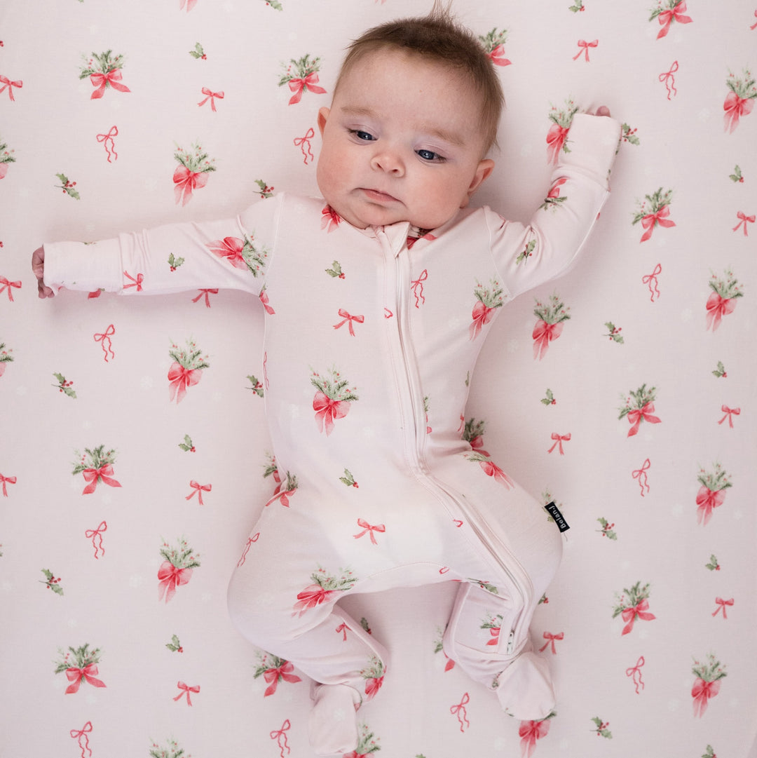 Baby wearing pink bows bamboo sleeper with cute holiday print of bows and holly.