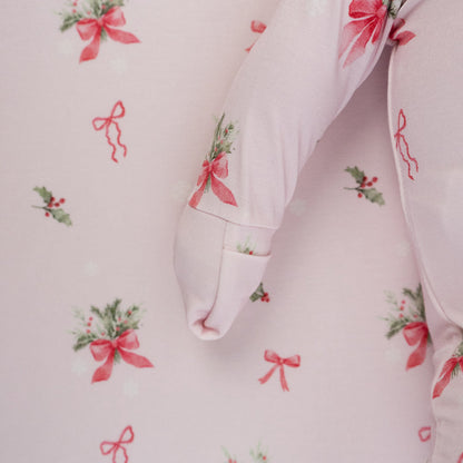 Close-up of pink bows bamboo sleeper featuring festive holly and whimsical snowflakes on a soft, pink background.