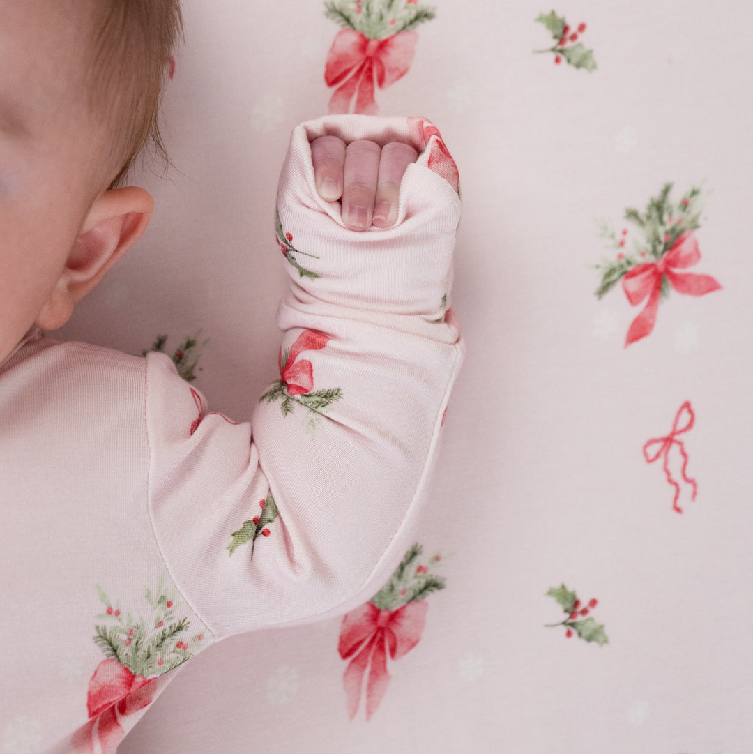 Infant wearing pink bows bamboo sleeper with festive holiday print and soft fabric for ultimate comfort.