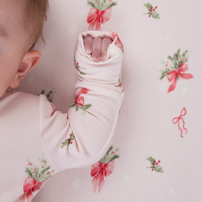Infant wearing pink bows bamboo sleeper with festive holiday print and soft fabric for ultimate comfort.
