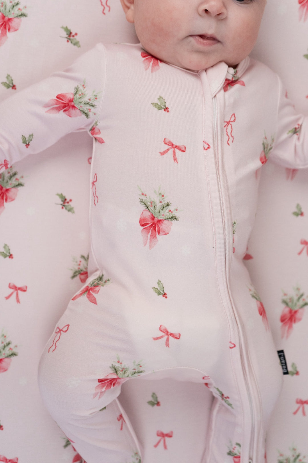 Adorable baby in pink bows bamboo sleeper with festive print of holly and snowflakes, perfect for the holidays.