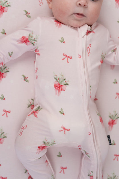 Adorable baby in pink bows bamboo sleeper with festive print of holly and snowflakes, perfect for the holidays.