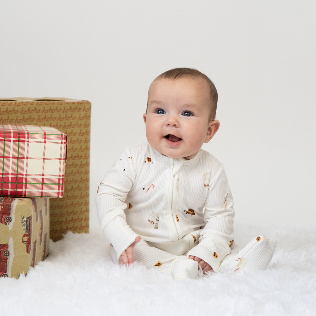 Baby smiling in a ribbed bamboo footless sleeper surrounded by festive holiday gifts.
