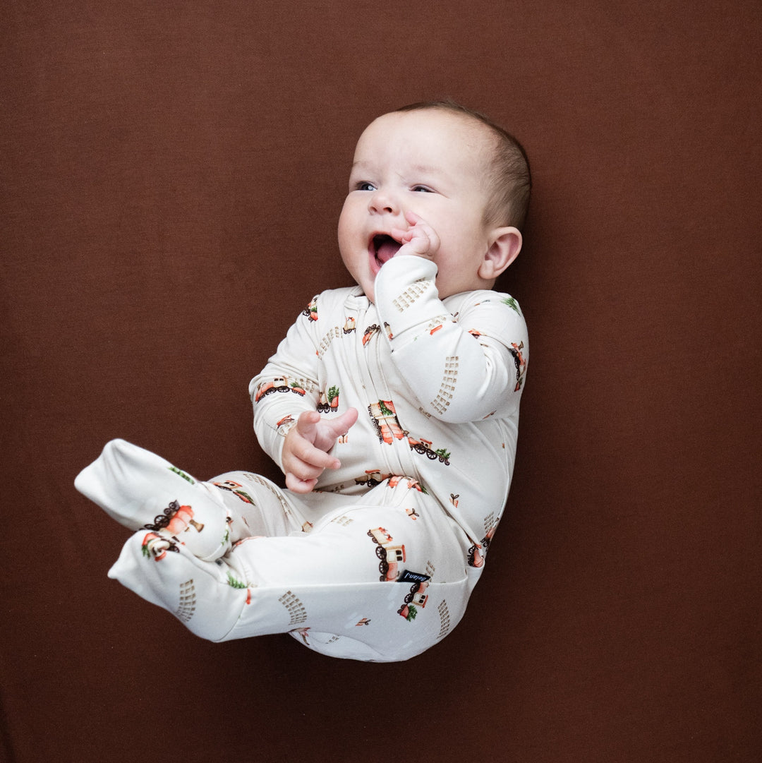 Baby in ribbed bamboo footless sleeper with festive cookies design, smiling on brown background.