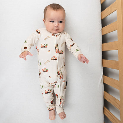 Baby wearing holiday bamboo footless sleeper with a Christmas train print in a crib.