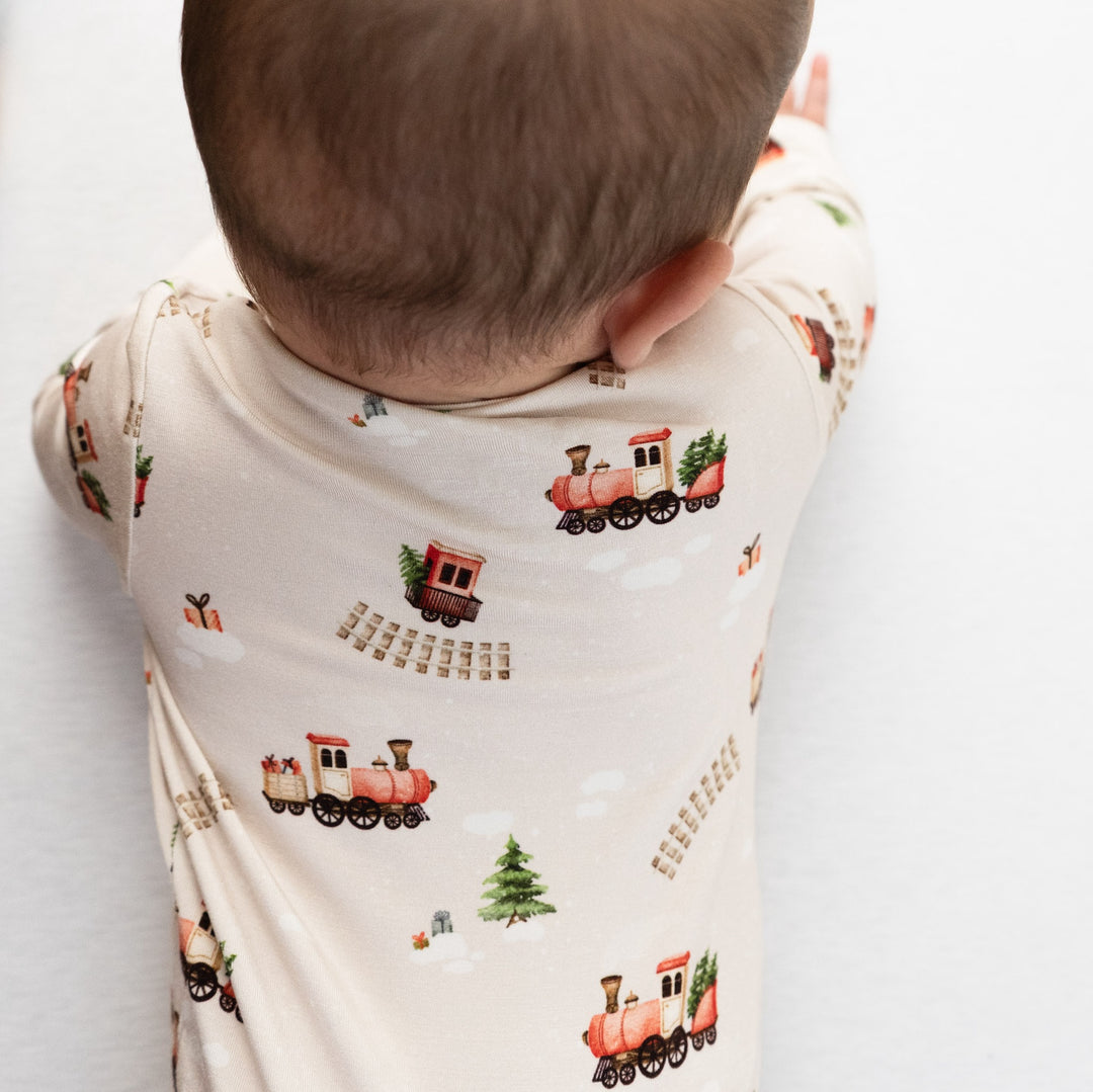 Baby in a footless zipper sleeper featuring a whimsical Christmas train print, perfect for a holiday bamboo footless sleeper.