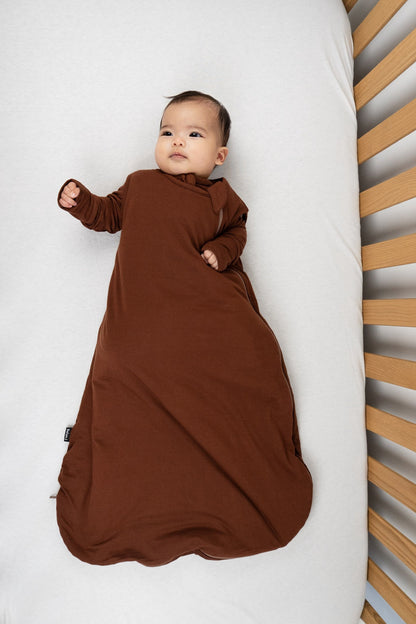 Baby peacefully resting in a cocoa bamboo sleep sack for babies on a crib mattress.