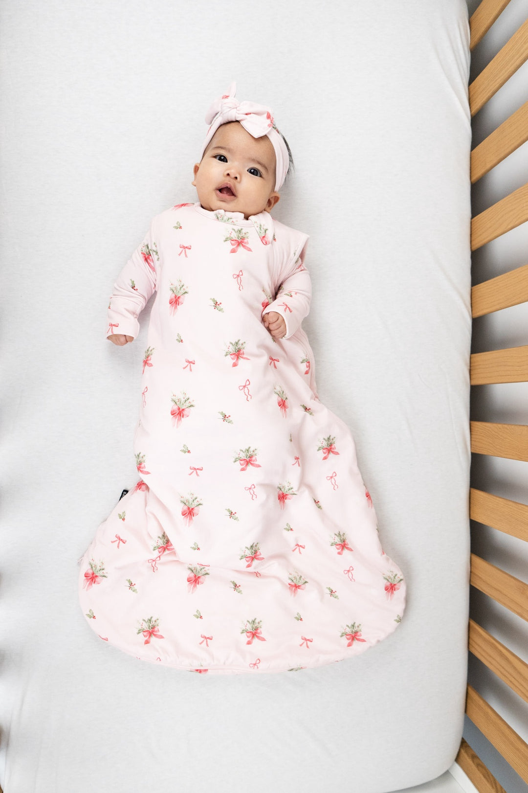 Baby in a pink bows sleep sack for babies, smiling and comfortably resting in a crib.