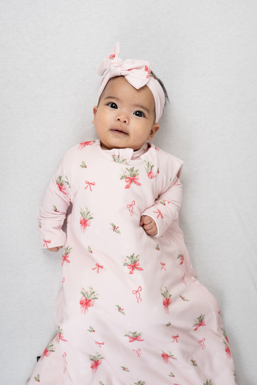 Baby wearing a pink bows sleep sack for babies with floral designs and a matching headband.