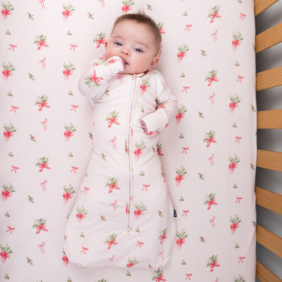 1.0 TOG convertible swaddle sack in pink bows design with baby in a crib.