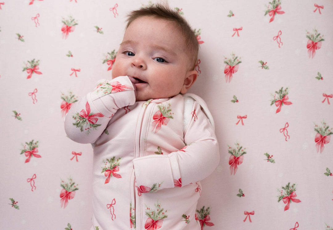 Baby wearing 1.0 TOG convertible swaddle sack with pink bows design, surrounded by matching patterned background.