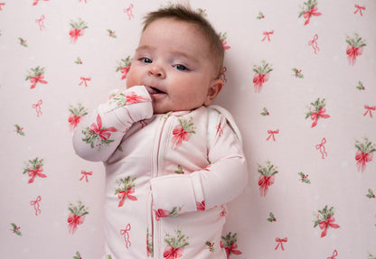 Baby wearing 1.0 TOG convertible swaddle sack with pink bows design, surrounded by matching patterned background.