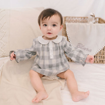 Baby wearing an organic cotton checker bodysuit with a classic check pattern, sitting on a bed.