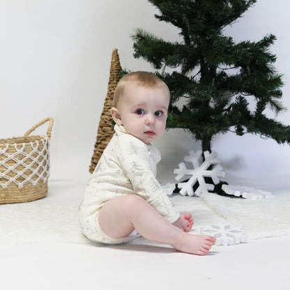 Baby wearing an organic cotton long sleeve bodysuit with polar bear print sitting by a Christmas tree.