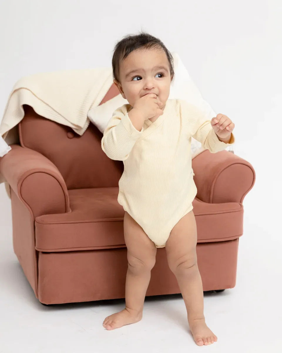 Baby in organic cotton bodysuit from the organic cotton baby gift set, sitting in a cozy chair.