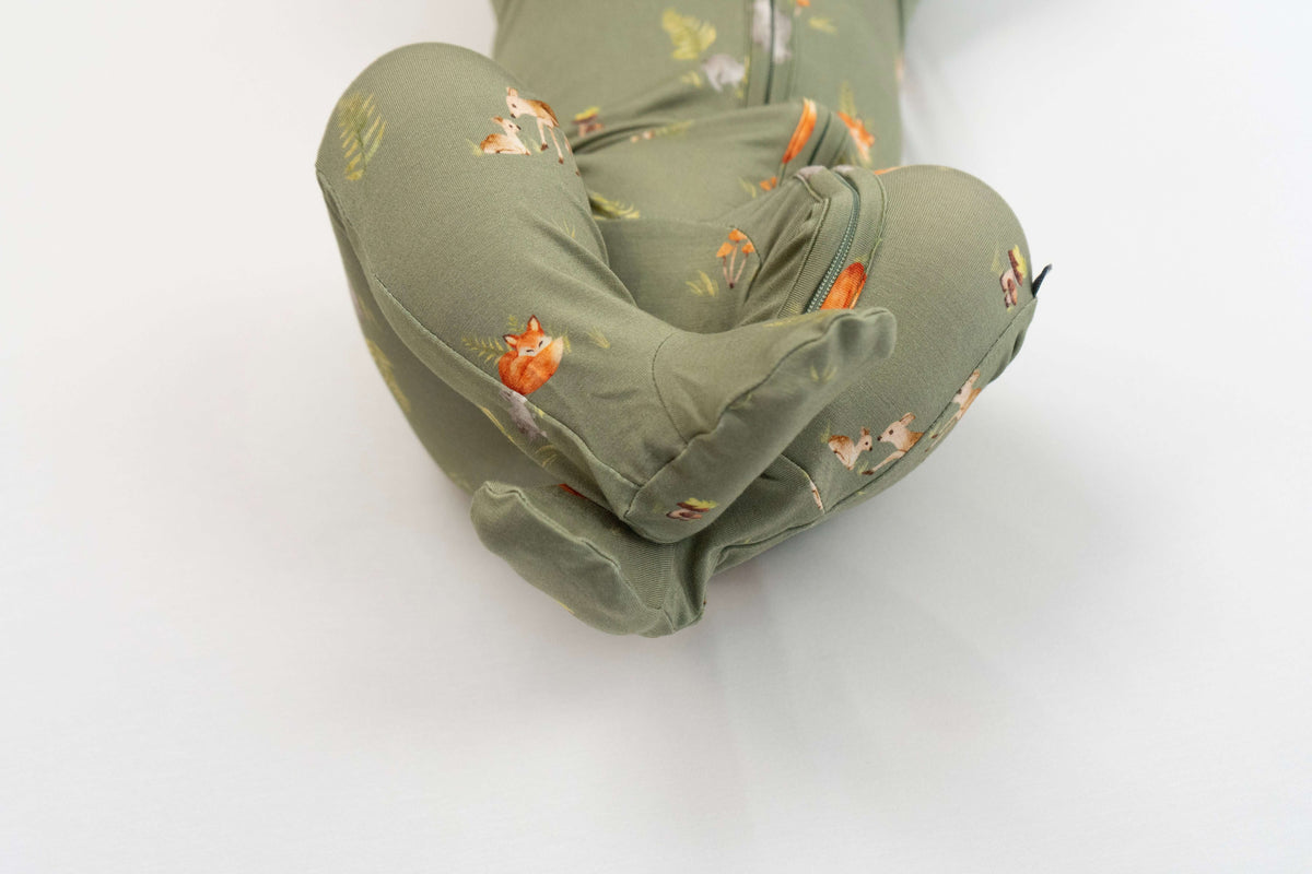 Forest friends footed zipper sleeper showing adorable animal prints on soft olive-green fabric.