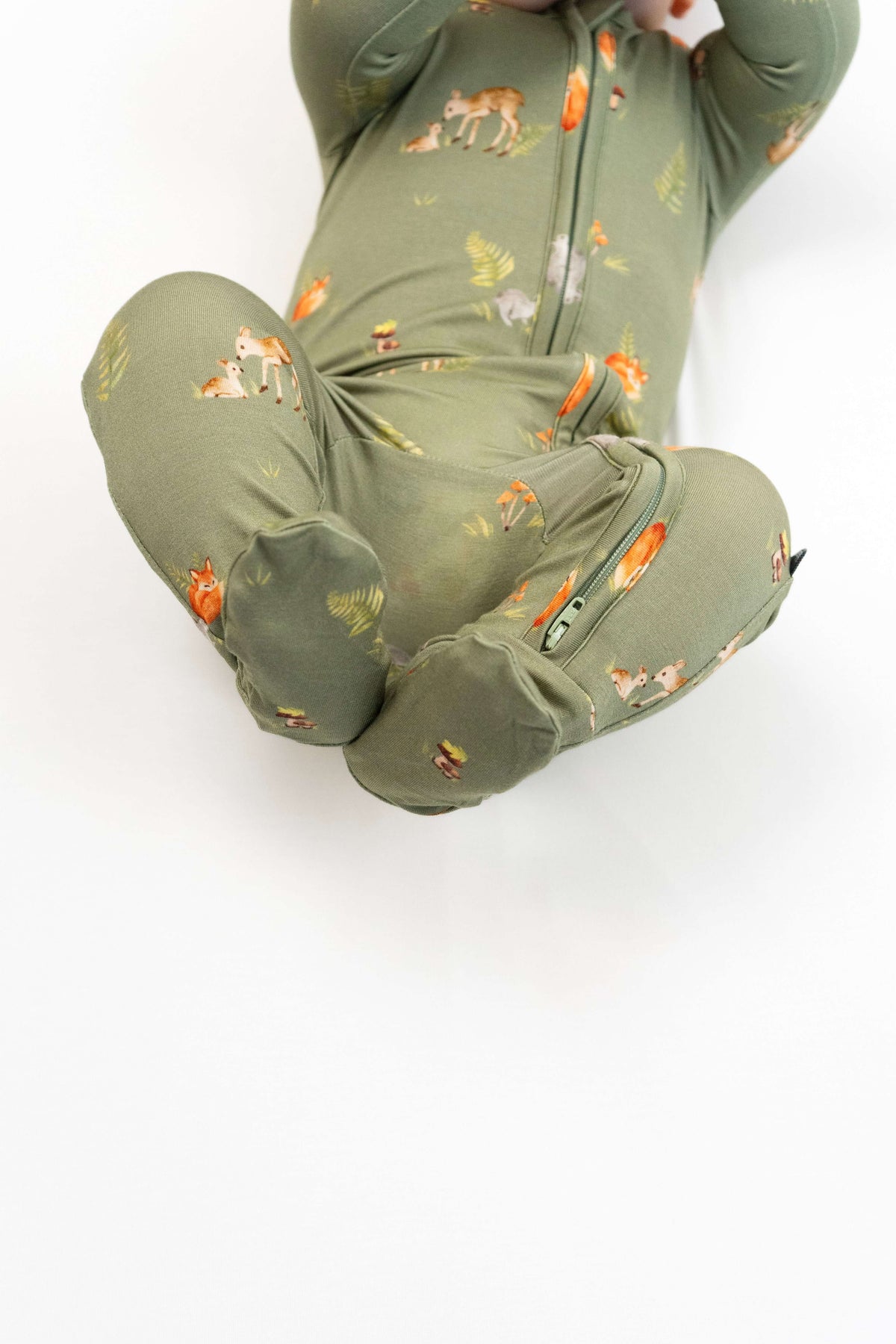 A child wearing the forest friends footed zipper sleeper featuring whimsical forest animals on a soft olive-green background.