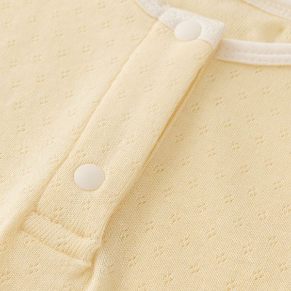 Close-up of the button detail on a creamy yellow organic cotton sleeveless baby bodysuit.